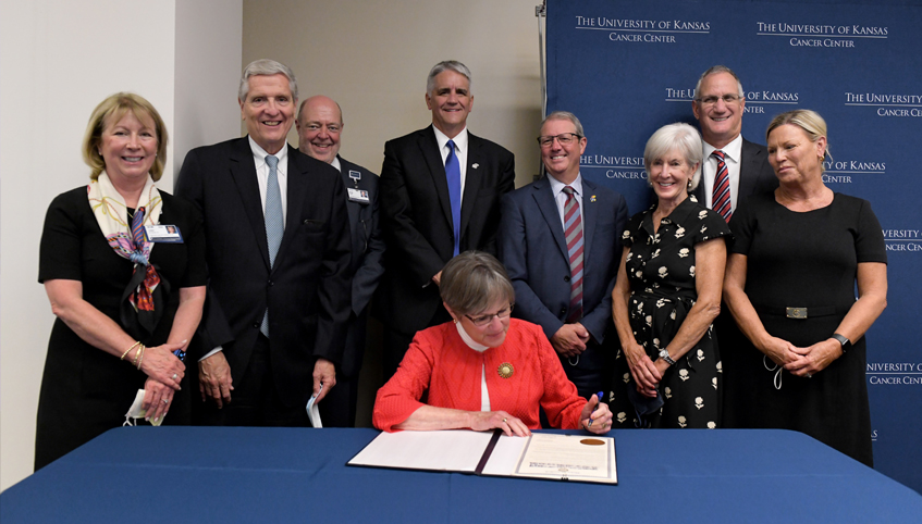 group of individuals surround governor kelly as she signs the proclamation