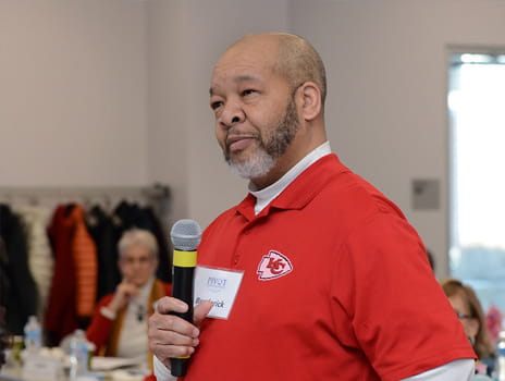 Black man with a grey bears speaks into a microphone